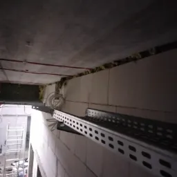 Metalowa korytka kablowa zamontowana na ścianie z bloczków w trakcie prac instalacyjnych w Nowym Mieście Lubawskim, widoczne przewody i drabina w tle.