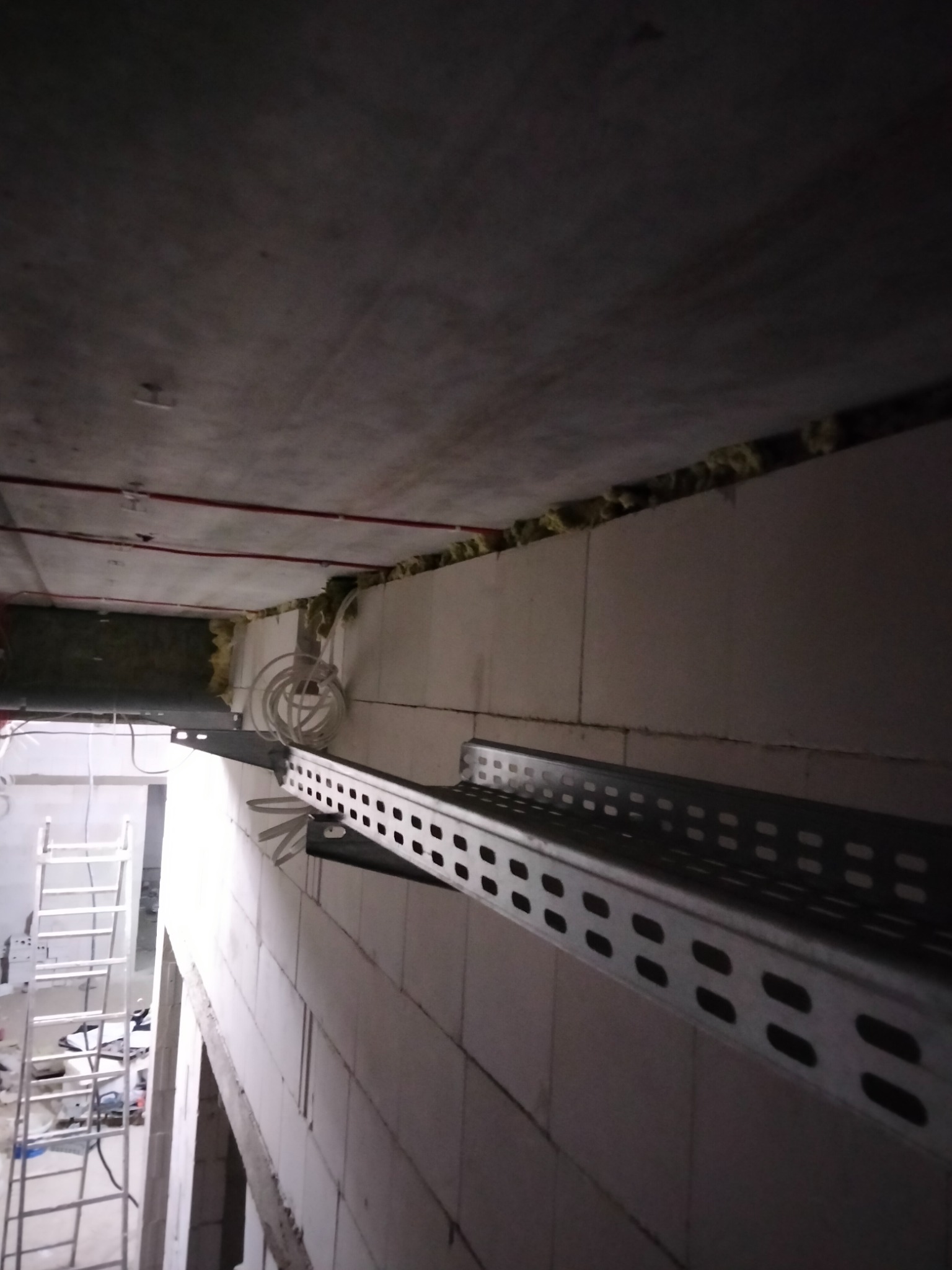 Metalowa korytka kablowa zamontowana na ścianie z bloczków w trakcie prac instalacyjnych w Nowym Mieście Lubawskim, widoczne przewody i drabina w tle.
