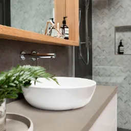 Nowoczesna łazienka w Murów z umywalką nablatową na blacie w odcieniach szarości, uzupełniona minimalistyczną armaturą i rośliną w szklanym wazonie.