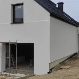 Nowoczesny dom jednorodzinny w Chojnicach po malowaniu elewacji na biało, widoczne rusztowania i pracownik przygotowujący się do dalszych prac wykończeniowych.