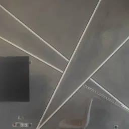 Szara ściana z geometrycznym wzorem z białych listew, telewizor na ścianie, krzesła w tle, widoczne gniazdka elektryczne.