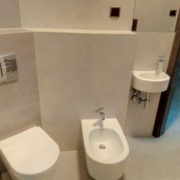 INCO - Nowoczesna łazienka z wiszącą toaletą, bidetem i umywalką, wykończona w jasnych, beżowych płytkach ceramicznych z minimalistycznymi akcentami.