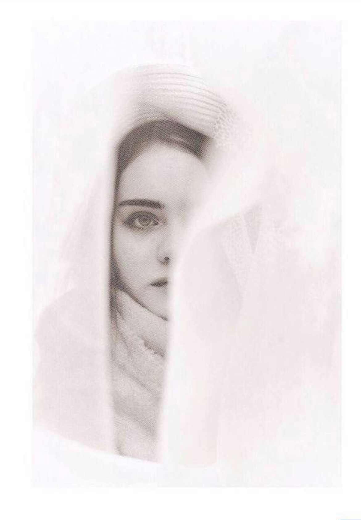 Portret kobiety z delikatnym makijażem, częściowo zasłoniętej przez białą, zwiewną tkaninę i kapelusz, w jasnej, minimalistycznej tonacji.