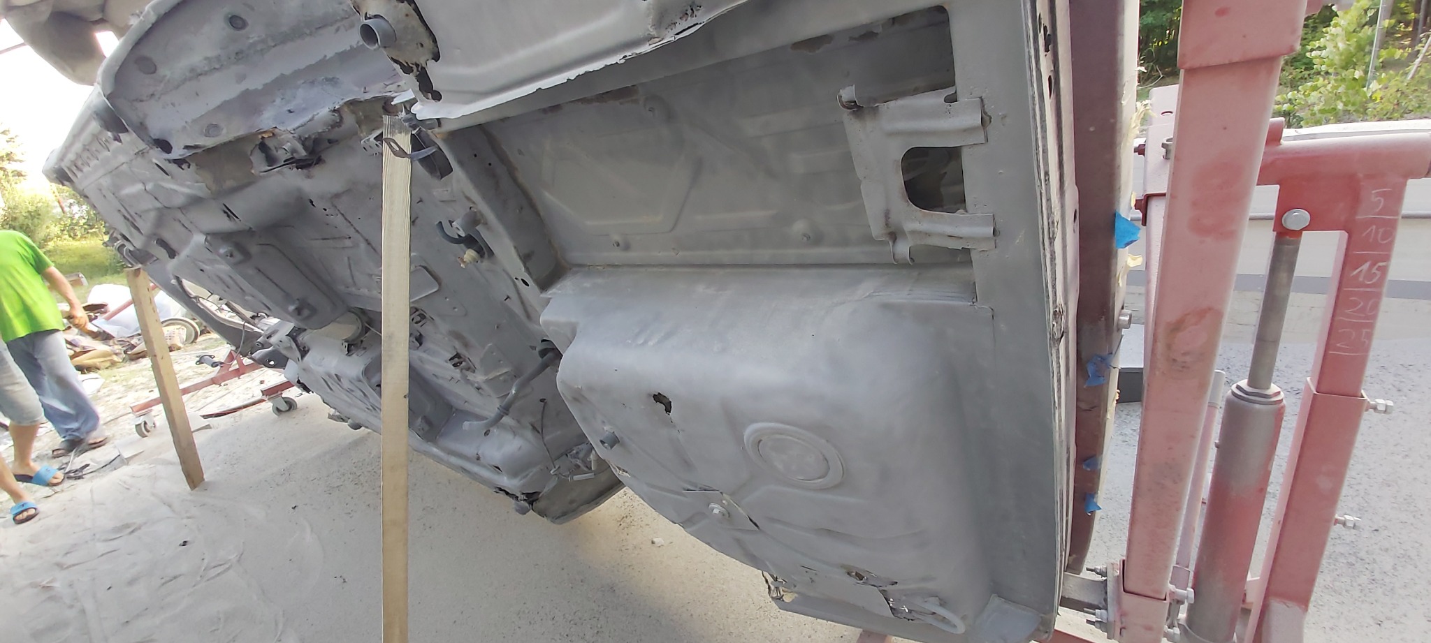 Podwozie samochodu po piaskowaniu, podniesione na podnośniku, widoczne ślady korozji i resztki farby, przygotowane do dalszych prac blacharskich.