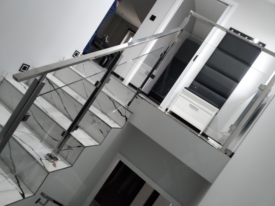 Schody z marmurowymi stopniami zabezpieczone szklaną balustradą z elementami ze stali nierdzewnej, widok z dołu.