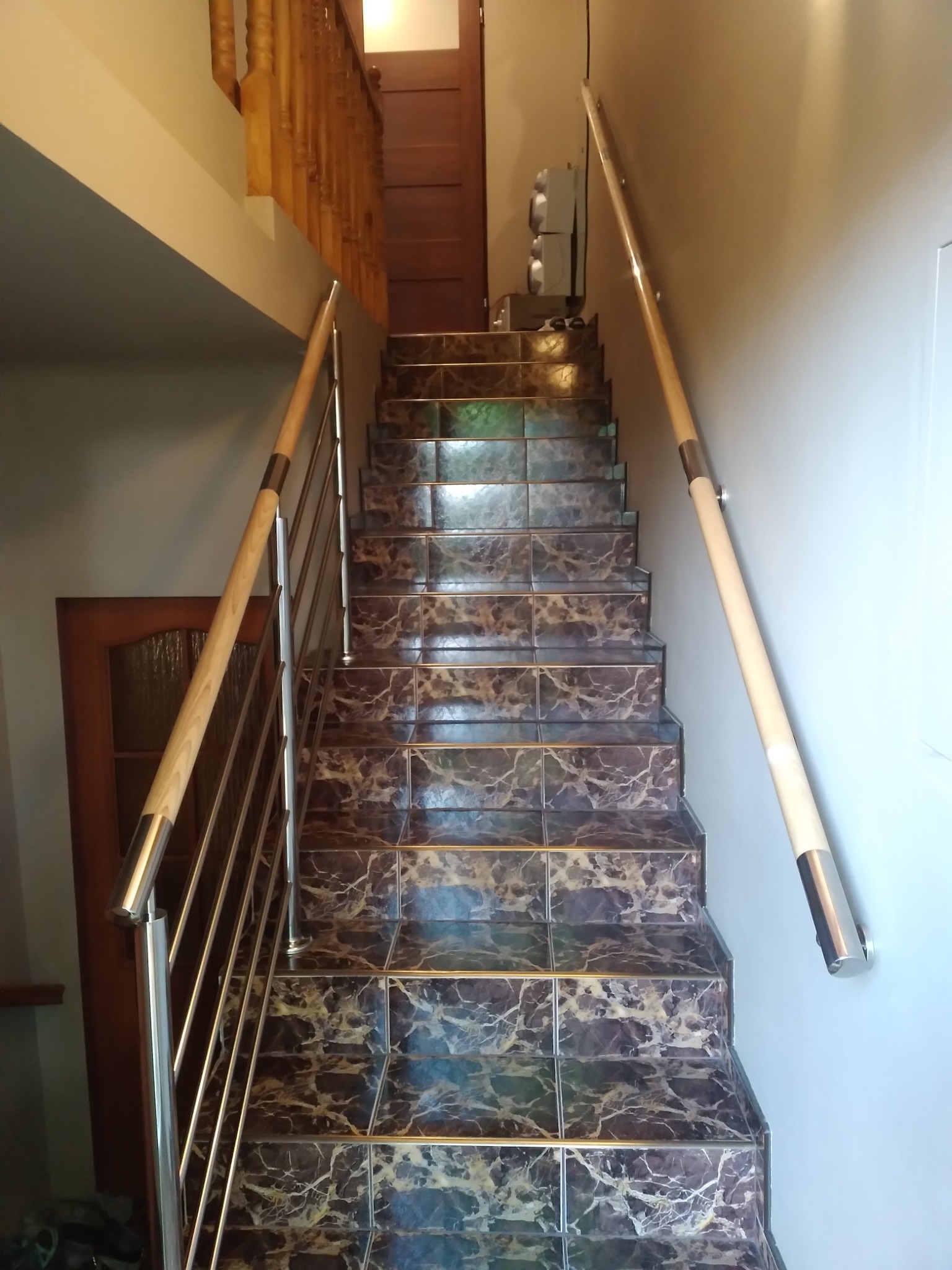 Schody wewnętrzne z marmurowymi płytkami, zabezpieczone metalową balustradą z drewnianą poręczą, widok z dołu.