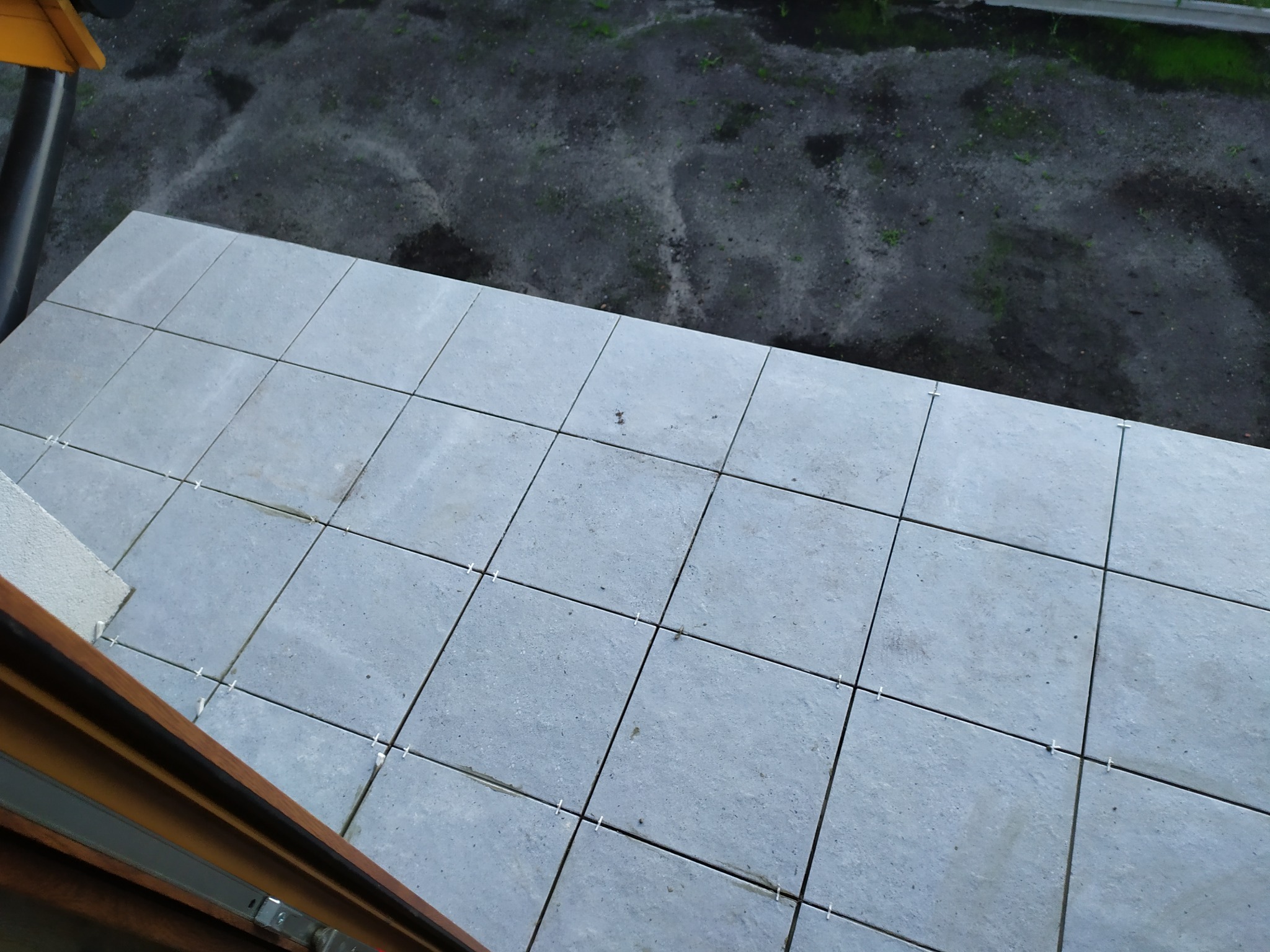 Ułożone szare płytki na balkonie z krzyżykami dystansowymi, widok z góry.