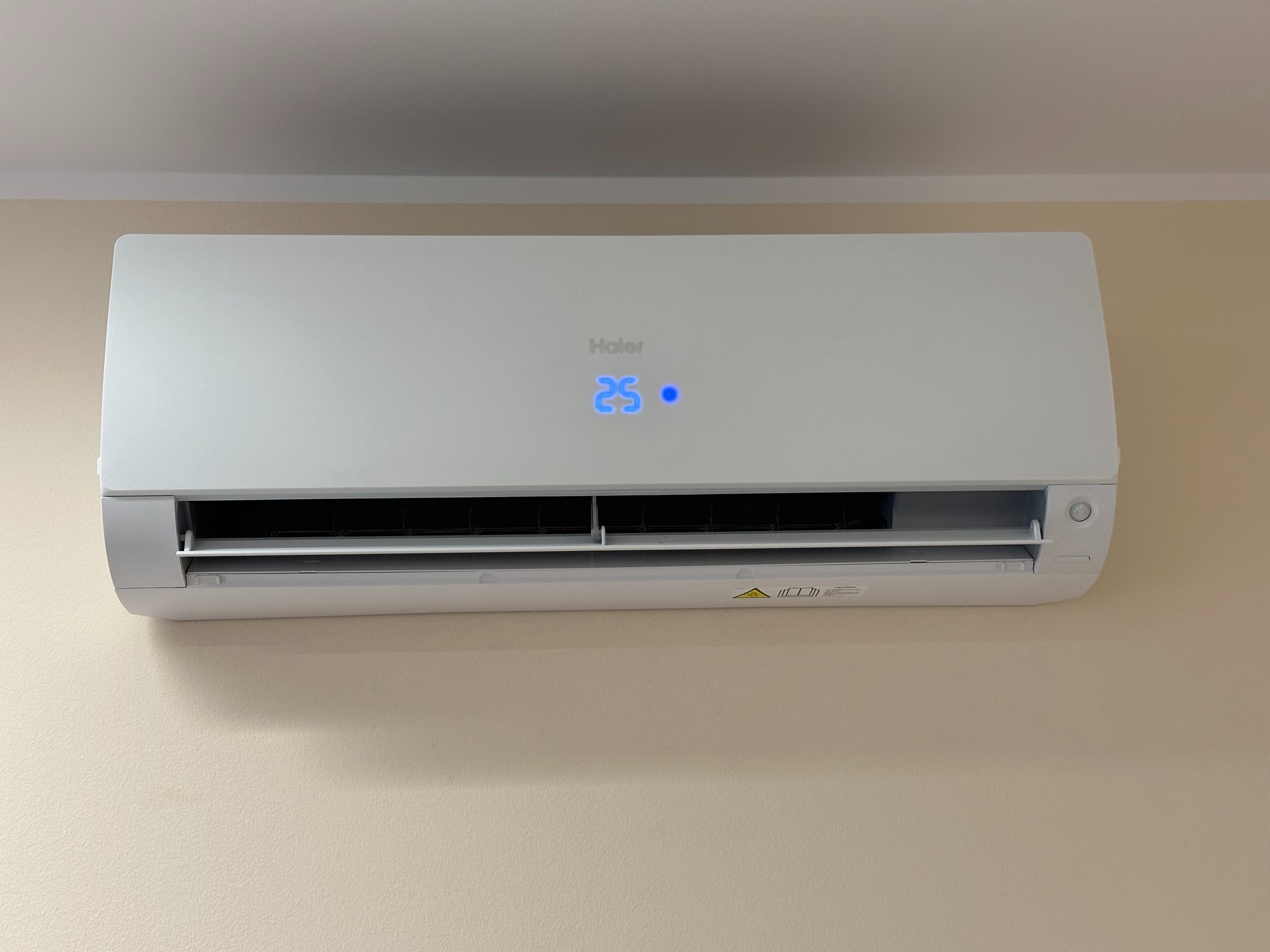 Świeżo zamontowana, biała klimatyzacja Haier w jasnym pomieszczeniu, wyświetlacz pokazuje 25 stopni.