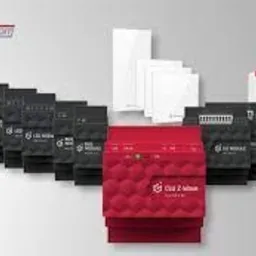 Zestaw komponentów inteligentnego domu marki Grenton, zawierający moduły sterujące, przekaźniki i czujniki, ułożone na jasnoszarym tle w formie piramidy. Widoczne logo producenta w lewym górnym rogu.