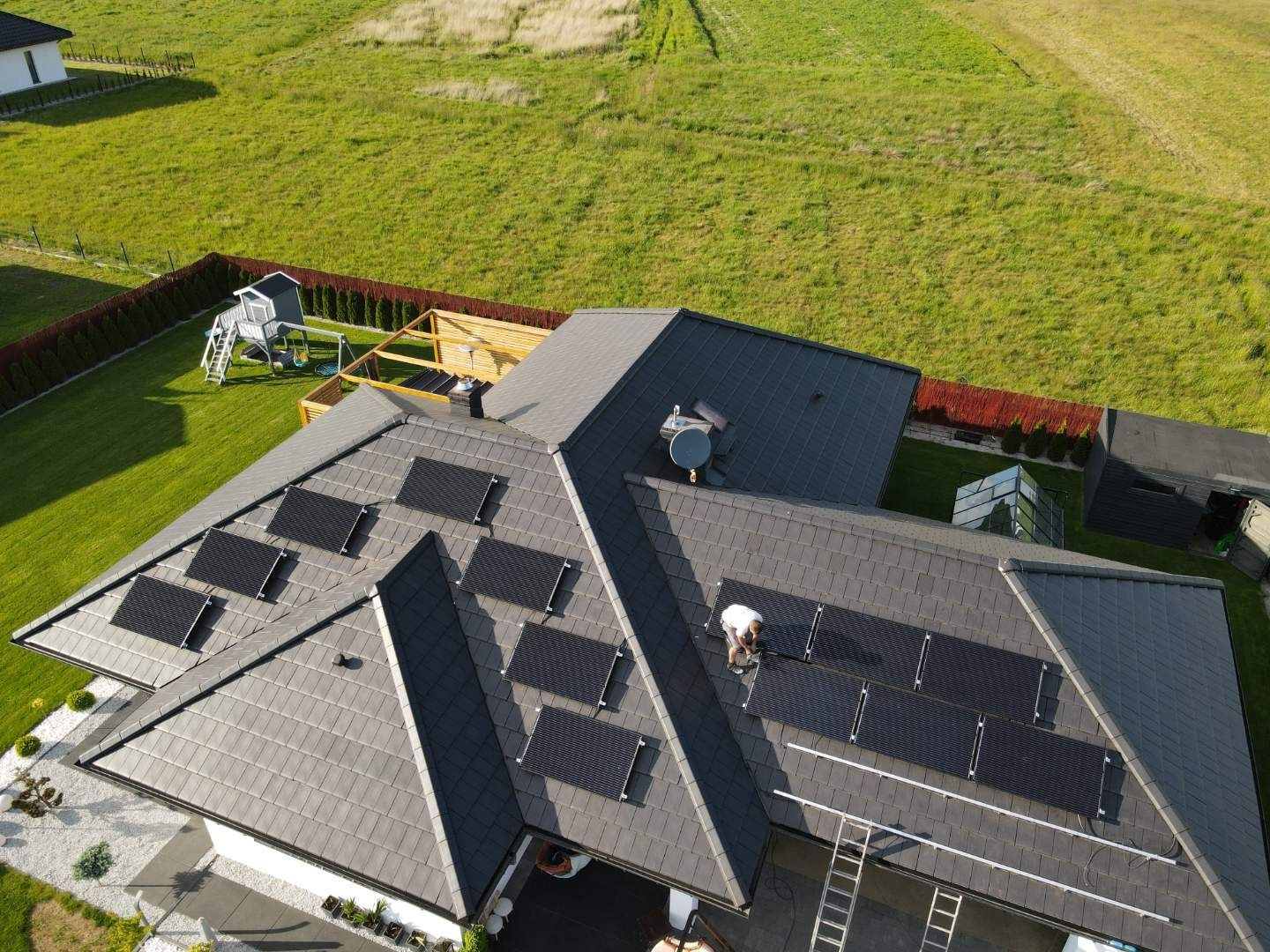 Montaż paneli słonecznych na dachu domu jednorodzinnego z szarej dachówki, widok z lotu ptaka, drabina oparta o dach.
