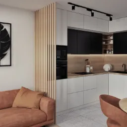 Wnętrze mieszkania: nowoczesna kuchnia z białymi i czarnymi szafkami, drewnianym blatem i panelami dekoracyjnymi, połączona z salonem z brązową sofą i obrazami z motywem liści.