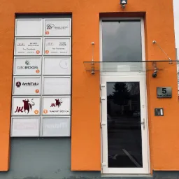 Pomarańczowy budynek z białymi ramkami zawierającymi nazwy firm, w tym 'Biuro Rachunkowe' i 'Eurobrokers', oraz numer budynku '5 Energetyków' obok białych drzwi wejściowych.