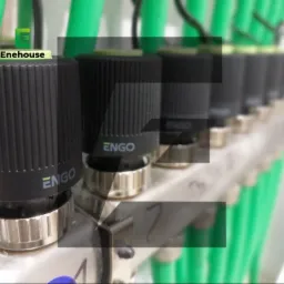 Rozdzielacz ogrzewania podłogowego z zielonymi rurami i czarnymi głowicami termostatycznymi ENGO, z numeracją obiegów. Widok z bliska, lekko rozmyte tło.