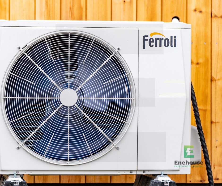 Biała pompa ciepła Ferroli na tle drewnianej ściany. Widoczny wentylator i logo Enehouse. Ujęcie z boku, podkreślające nowoczesny design i energooszczędność urządzenia.
