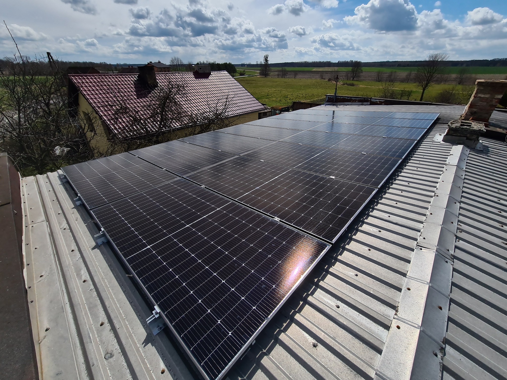 Panele słoneczne na blaszanym dachu domu z ceglanym kominem w słoneczny dzień, widok z góry.