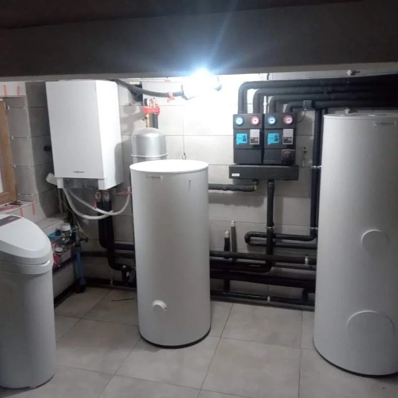 Kotłownia z dwoma białymi zbiornikami akumulacyjnymi, kotłem grzewczym Viessmann, stacją uzdatniania wody i rozbudowaną instalacją rurową z izolacją termiczną.