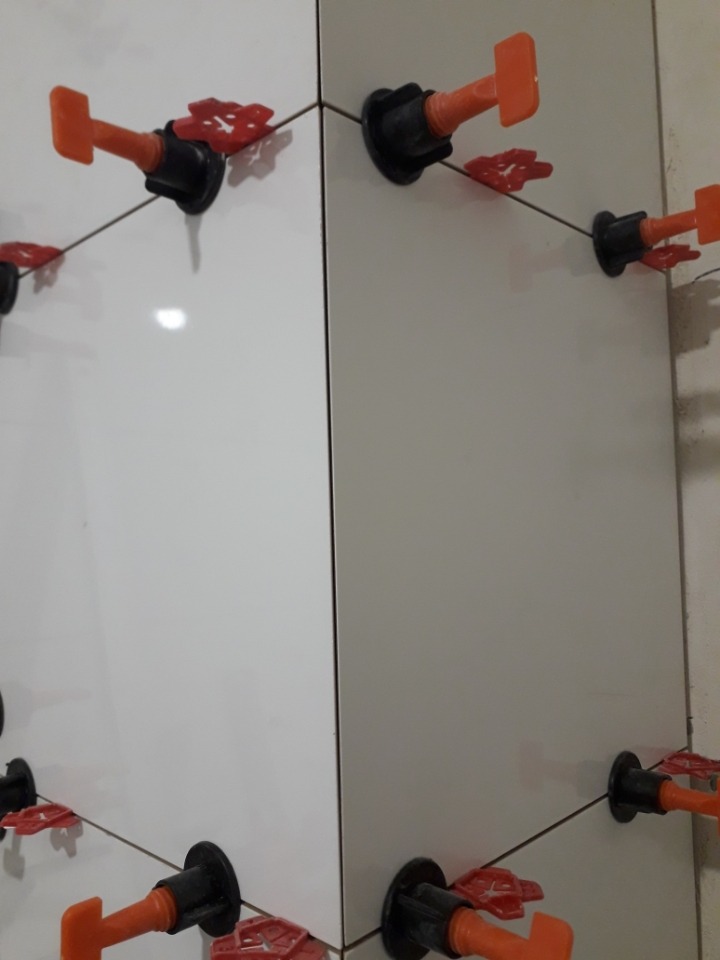 Ułożone białe płytki z pomarańczowymi klinami poziomującymi na ścianie.