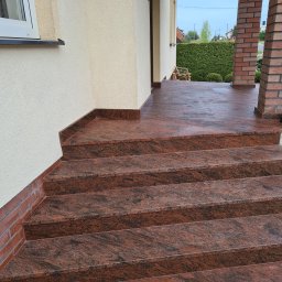 Mountain Stone Kamieniarstwo - Zewnętrzne schody wejściowe wyłożone czerwono-brązowym kamieniem z wyraźnym użyleniem, prowadzące na taras z ceglanymi filarami.