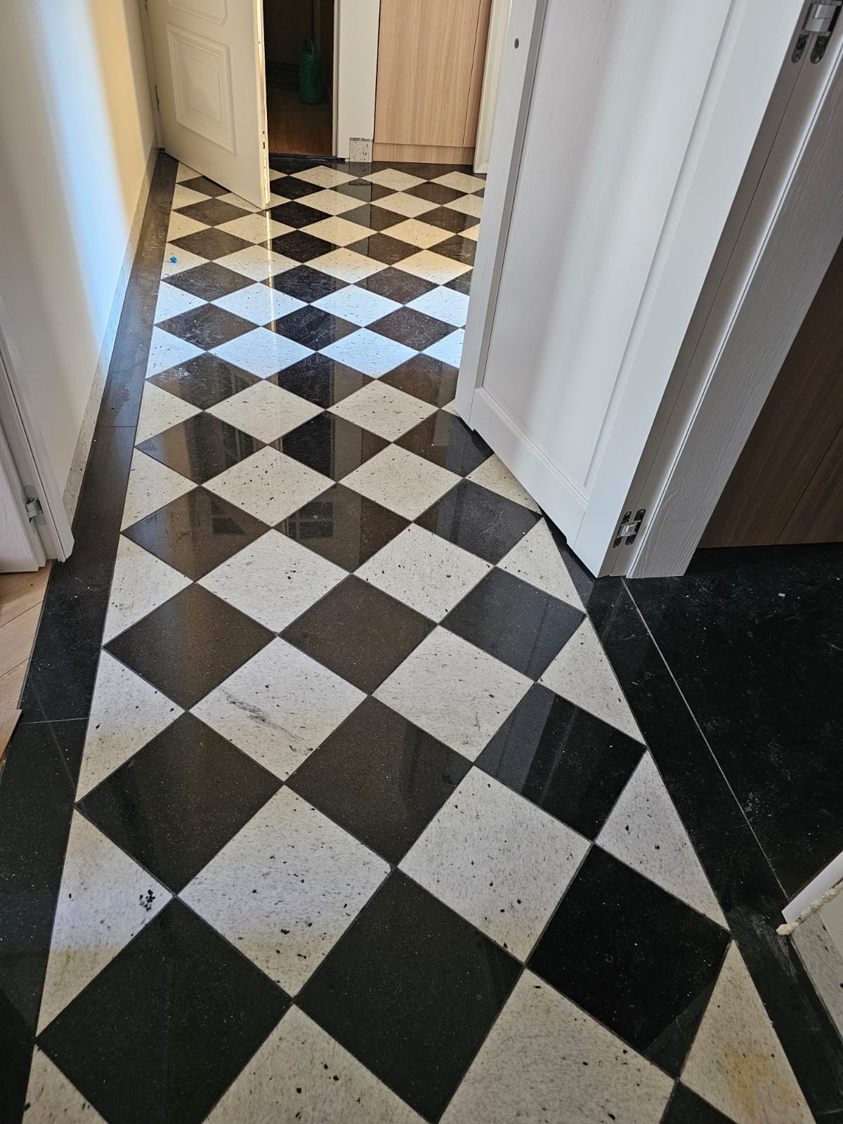 Podłoga w korytarzu w Kolbudach wyłożona czarno-białą szachownicą z kamienia, widok z perspektywy wejścia, z otwartymi białymi drzwiami po bokach.