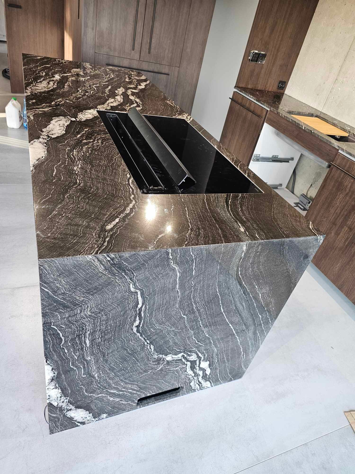 Czarno-biały blat kuchenny z kamienia o falistym wzorze, z wbudowaną płytą indukcyjną i pochłaniaczem oparów, w nowoczesnej kuchni z drewnianymi szafkami.