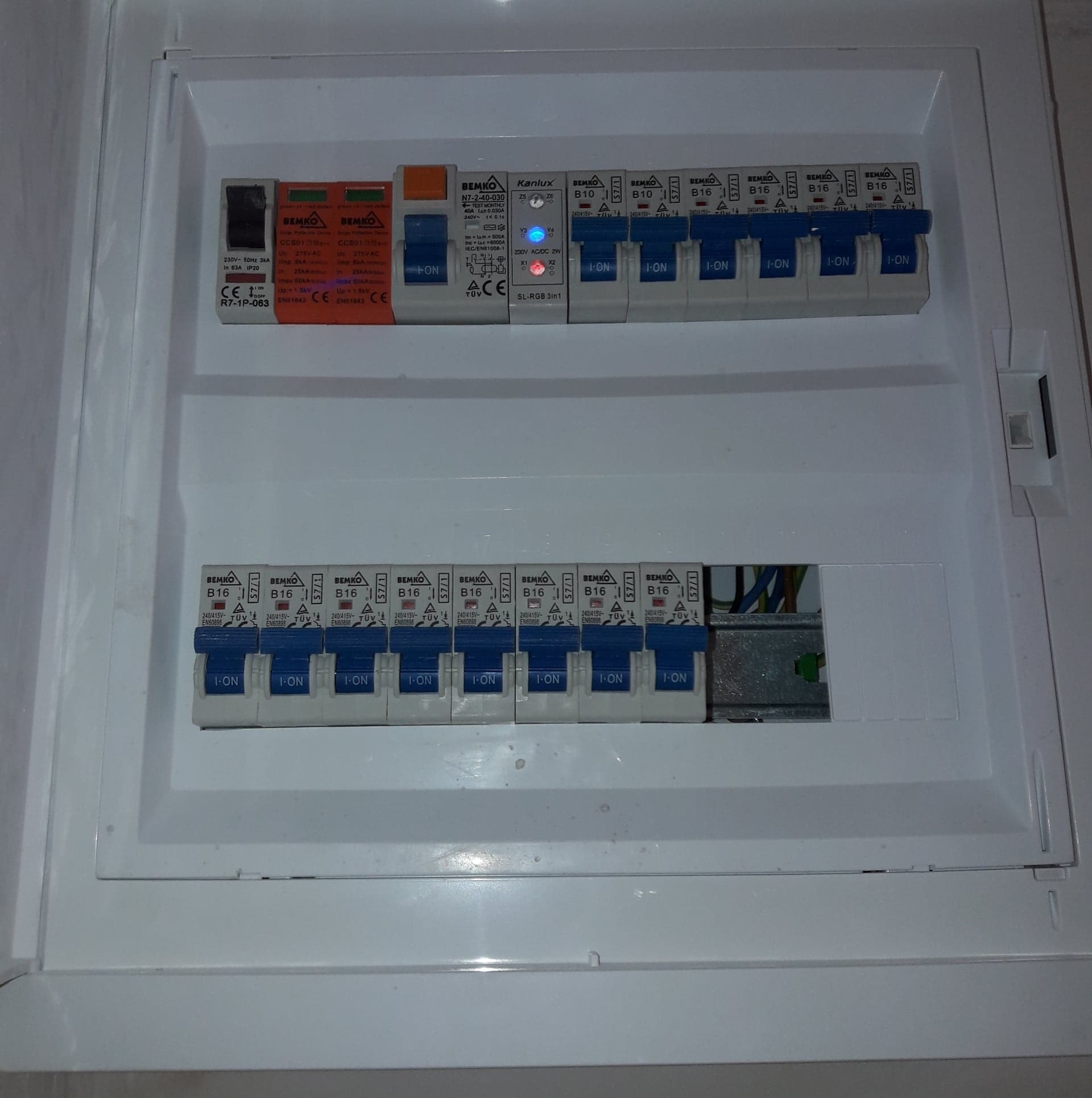 Otwarta skrzynka rozdzielcza z zainstalowanymi bezpiecznikami automatycznymi Bemko i Kanlux, widoczne przewody elektryczne.