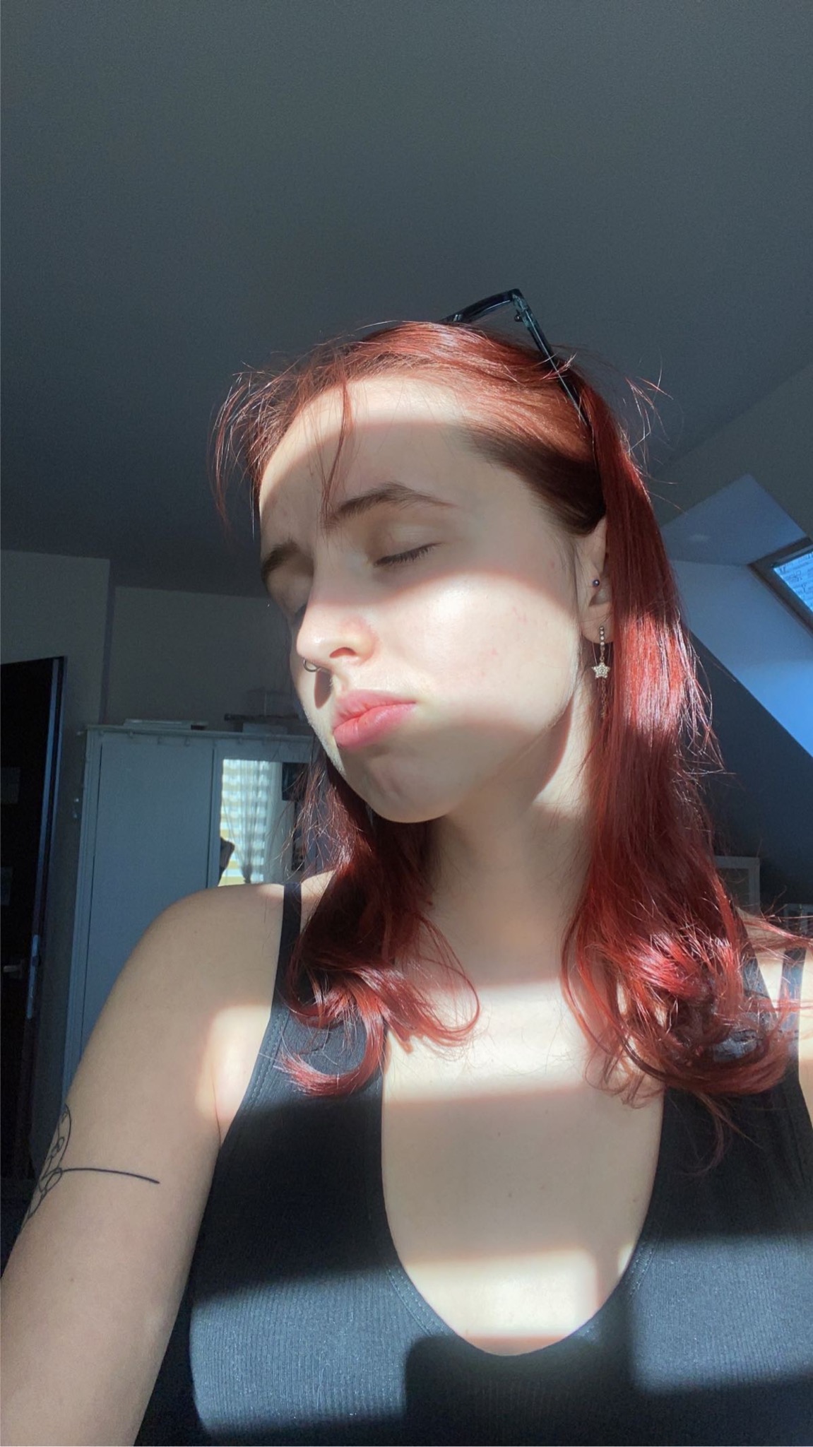 Portret młodej kobiety z rudymi włosami i kolczykiem w kształcie gwiazdy, oświetlonej promieniami słońca wpadającymi przez okno.