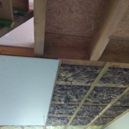 MIREMO usługi remontowo-budowlane - Montaż izolacji stropu wełną mineralną pomiędzy drewnianymi belkami, częściowo zakrytej płytą gipsowo-kartonową, widok od dołu.