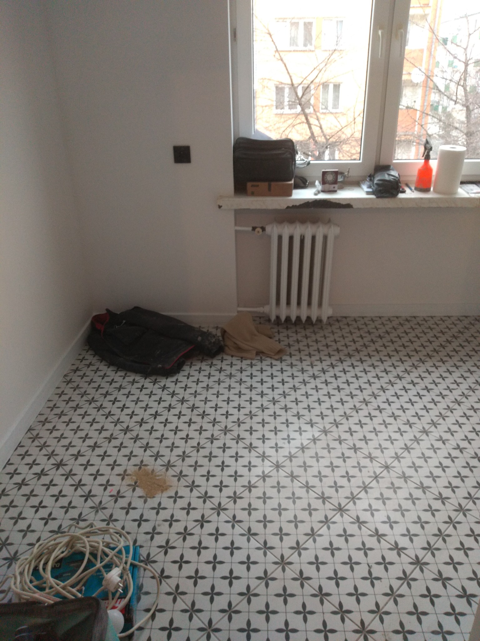 Nowo położona, wzorzysta podłoga w pokoju z grzejnikiem i oknem, widoczne ślady po fugowaniu i nieuprzątnięte narzędzia.