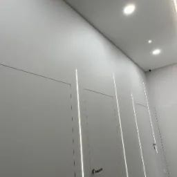 Nowoczesne oświetlenie LED w korytarzu biurowym w Łodzi, z minimalistycznymi białymi drzwiami i ukrytymi źródłami światła.