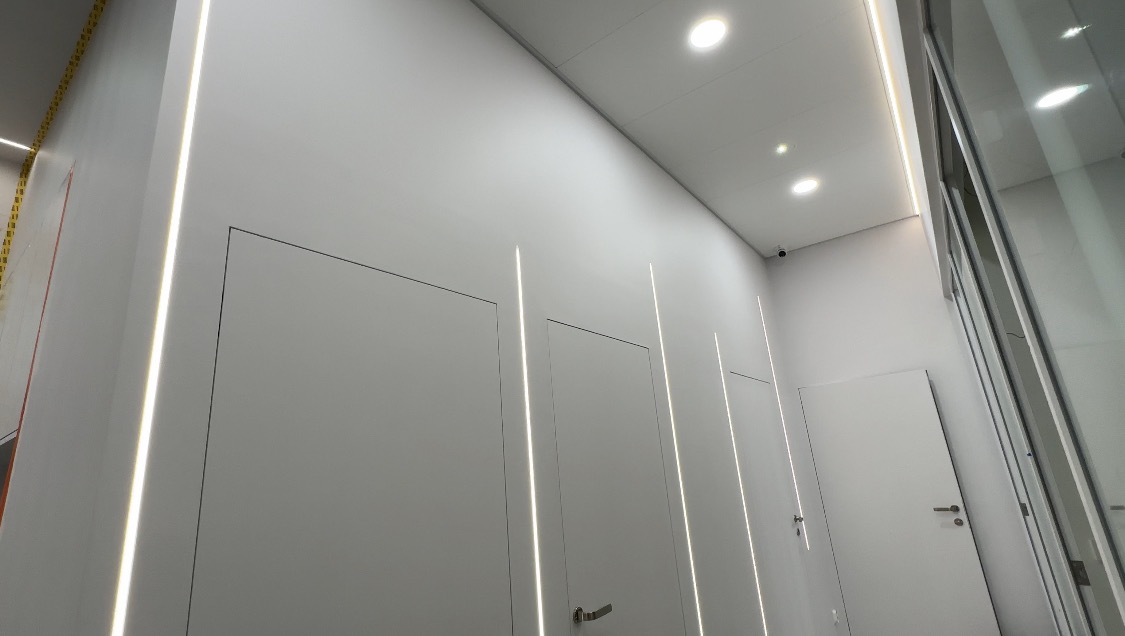 Nowoczesne oświetlenie LED w korytarzu biurowym w Łodzi, z minimalistycznymi białymi drzwiami i ukrytymi źródłami światła.
