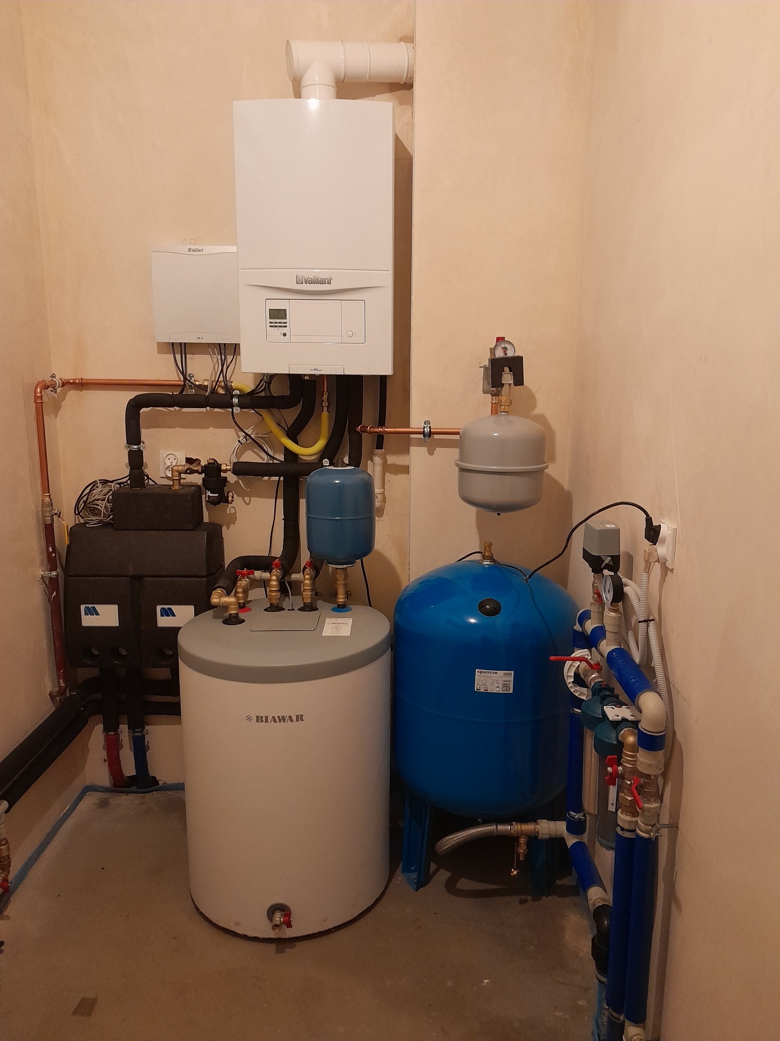 Instalacja kotła gazowego Vaillant, zbiornika Biawar i pompy Aquasystem w kotłowni z beżowymi ścianami.