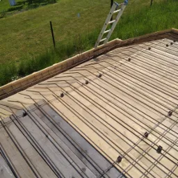 Przygotowanie szalunku i zbrojenia pod wylewkę fundamentową z widoczną drabiną opartą o ogrodzenie i zielony trawnik w tle.