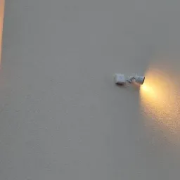 Elewacja budynku z zamontowanymi dwoma rodzajami oświetlenia zewnętrznego: kinkietem w kształcie tuby oraz reflektorem punktowym z czujnikiem ruchu.