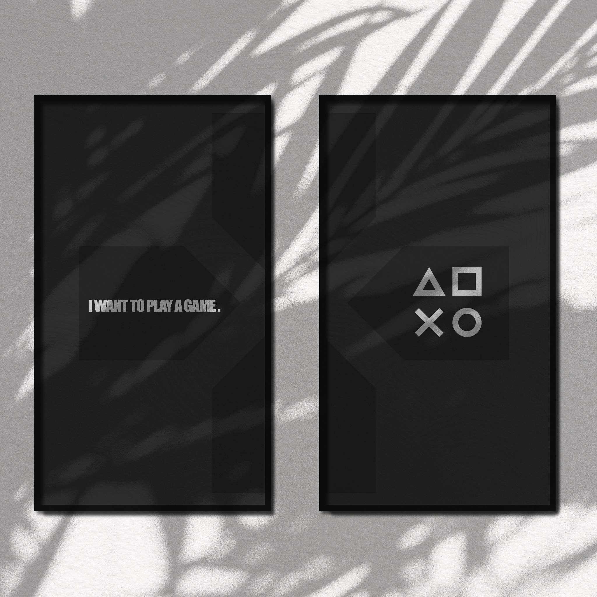 Dwa czarne plakaty w ramkach z motywem gamingowym: napis 'I WANT TO PLAY A GAME' na jednym i symbolami kontrolera na drugim, oświetlone cieniem liści na białej ścianie.