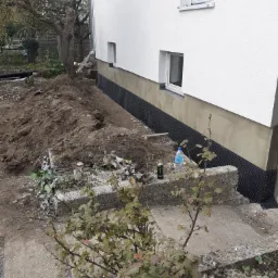 Przygotowanie do izolacji fundamentów budynku, widoczna membrana kubełkowa, obok wykopana ziemia, butelka wody i puszka napoju energetycznego.