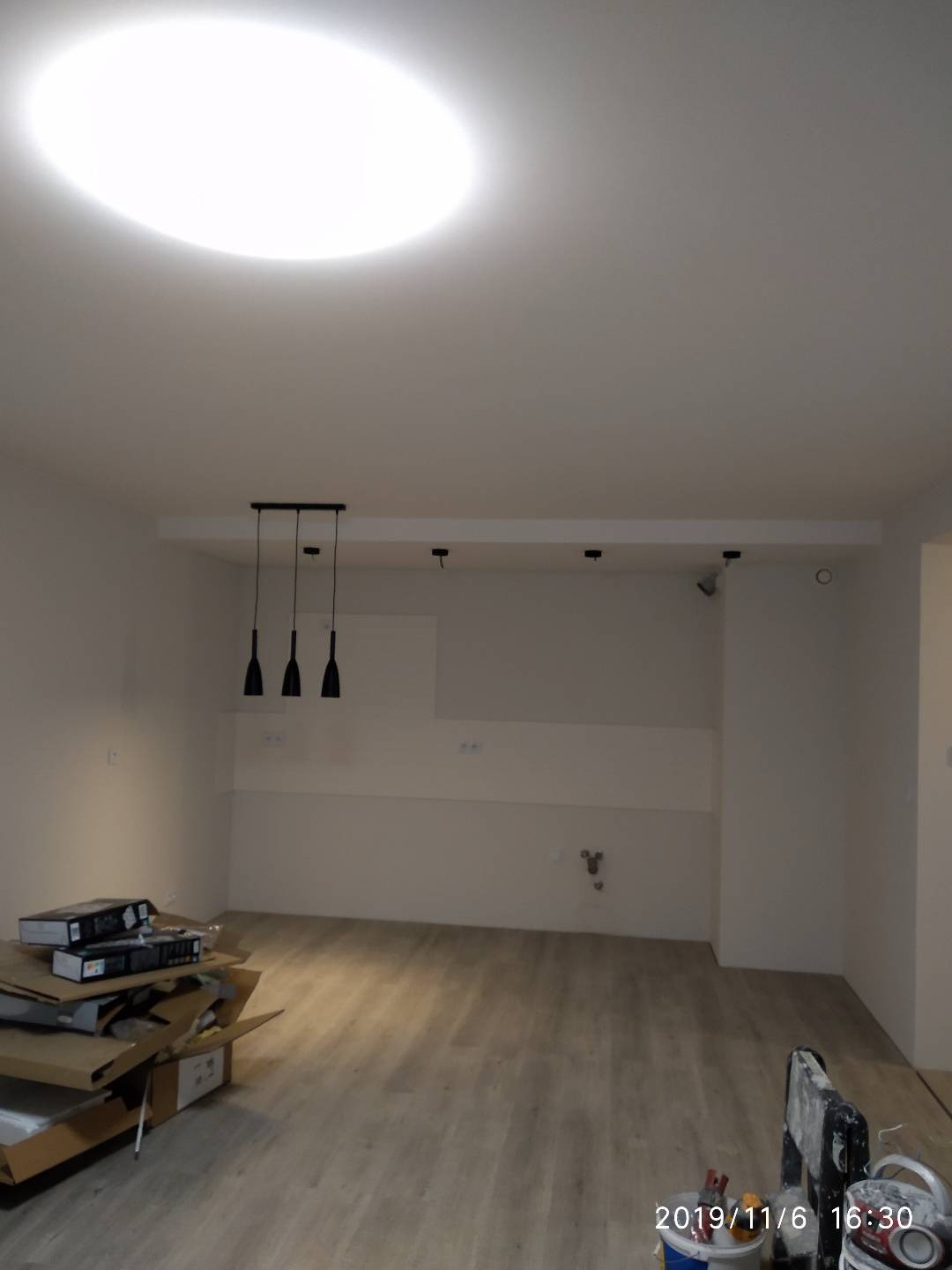 Wnętrze pokoju po remoncie z ułożonymi panelami podłogowymi, widoczne kartony po panelach, drabina malarska i lampy sufitowe.