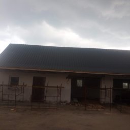 CHMUR-DACH Damian Chmura - Budynek gospodarczy z nowym, ciemnym dachem z blachy trapezowej, widoczne rusztowania i przygotowane deski, pochmurne niebo.