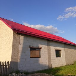 CHMUR-DACH Damian Chmura - Świeżo położony, jaskrawoczerwony dach z blachy trapezowej na budynku z białych bloczków, częściowo otynkowanym, z widocznym stosem starych płyt eternitowych u podstawy ściany