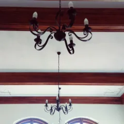 Odrestaurowany sufit z drewnianymi belkami i dekoracyjnymi, geometrycznymi malowidłami w kolorze złota, widoczne dwa żyrandole w stylu retro.