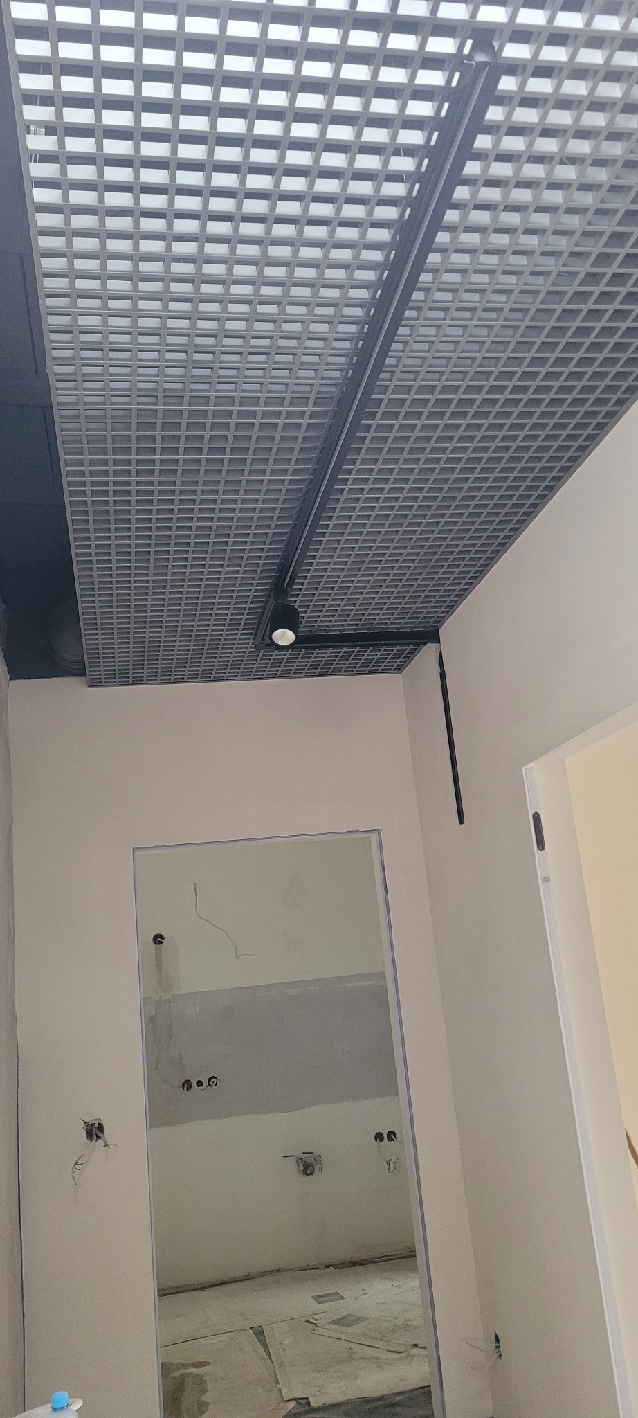 Sufit rastrowy z zamontowanym punktowym oświetleniem szynowym w pomieszczeniu w trakcie remontu, widoczne wystające kable elektryczne.