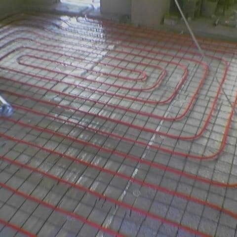 Czerwone rurki ogrzewania podłogowego ułożone na metalowej siatce zalewane wylewką betonową.