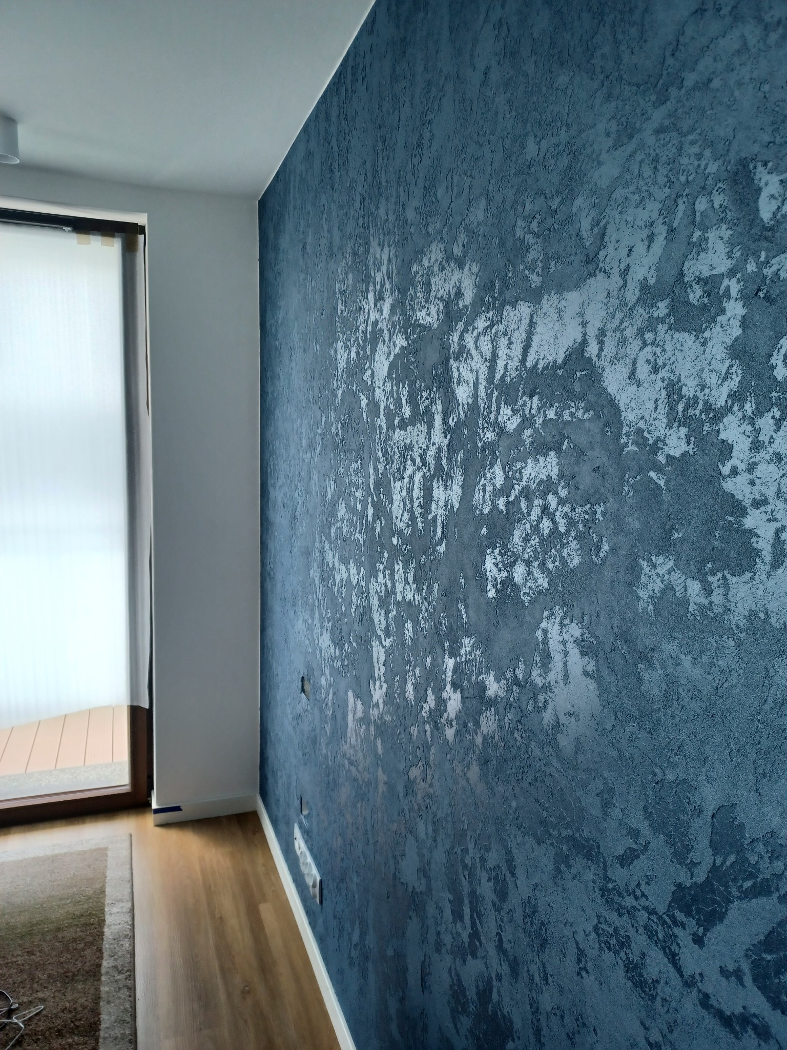 Dekoracyjna ściana w odcieniach granatu i srebra z efektem strukturalnym, widoczna z boku w nowoczesnym wnętrzu z drewnianą podłogą i oknem.