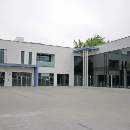 Nowoczesny budynek biurowy z dużymi oknami i szarym brukowanym placem przed wejściem, tabliczka adresowa 11a widoczna na rogu budynku.