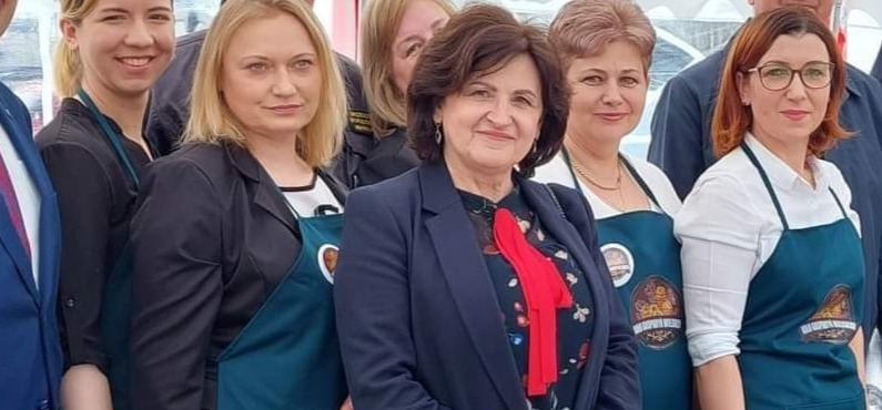 Grupowe portretowe ujęcie kobiet w fartuchach z logo, prawdopodobnie podczas wydarzenia firmowego lub promocyjnego.