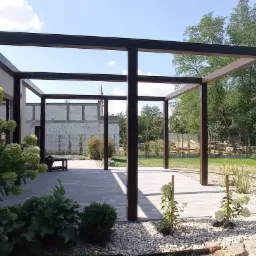 Nowoczesna, minimalistyczna pergola z ciemnego drewna na tarasie z szarej kostki, otoczona zielenią i białymi kamieniami, w tle budynek w trakcie budowy.