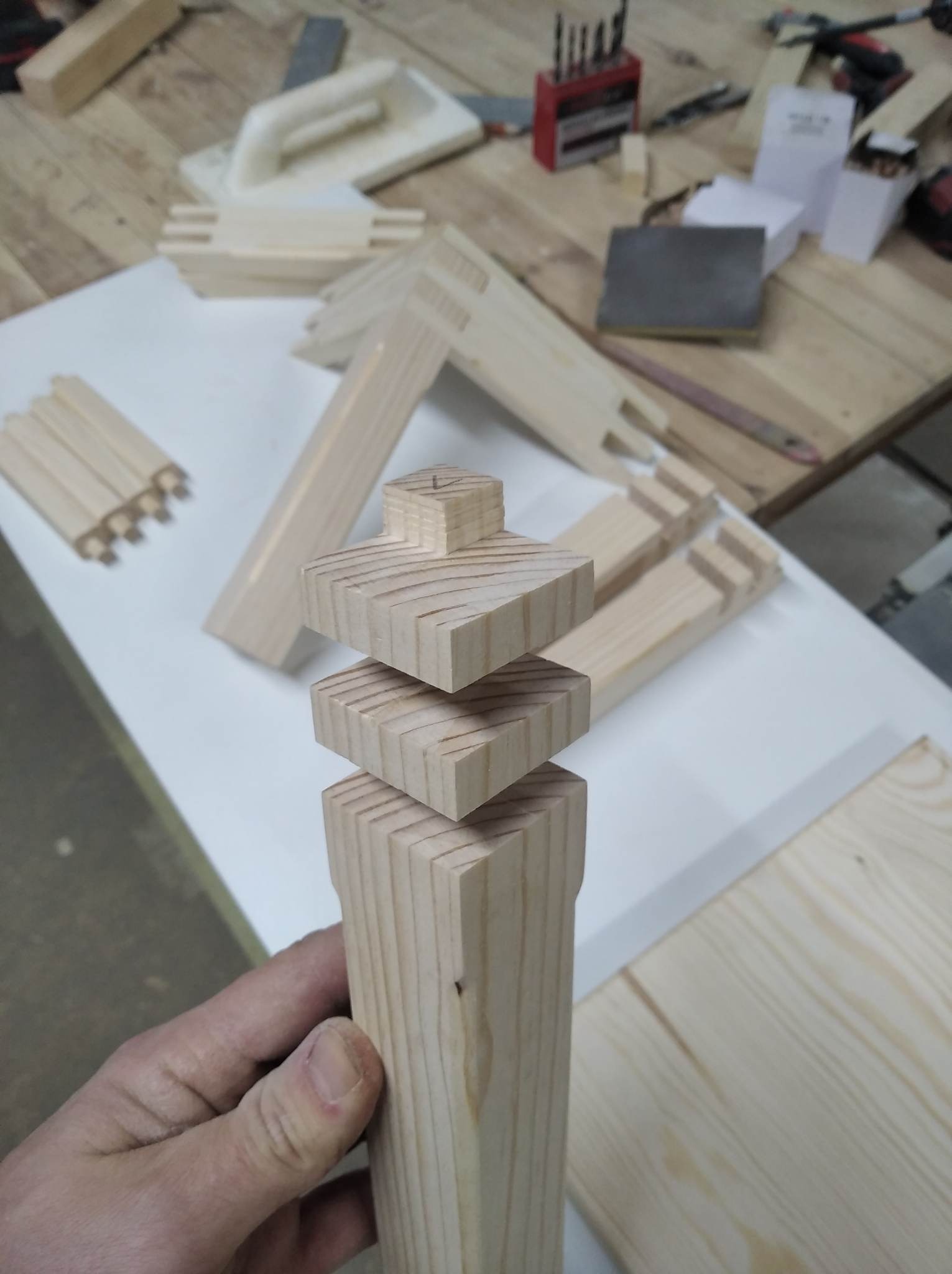 Drewniana noga meblowa w trakcie obróbki, z widocznymi elementami składowymi i narzędziami stolarskimi w tle.