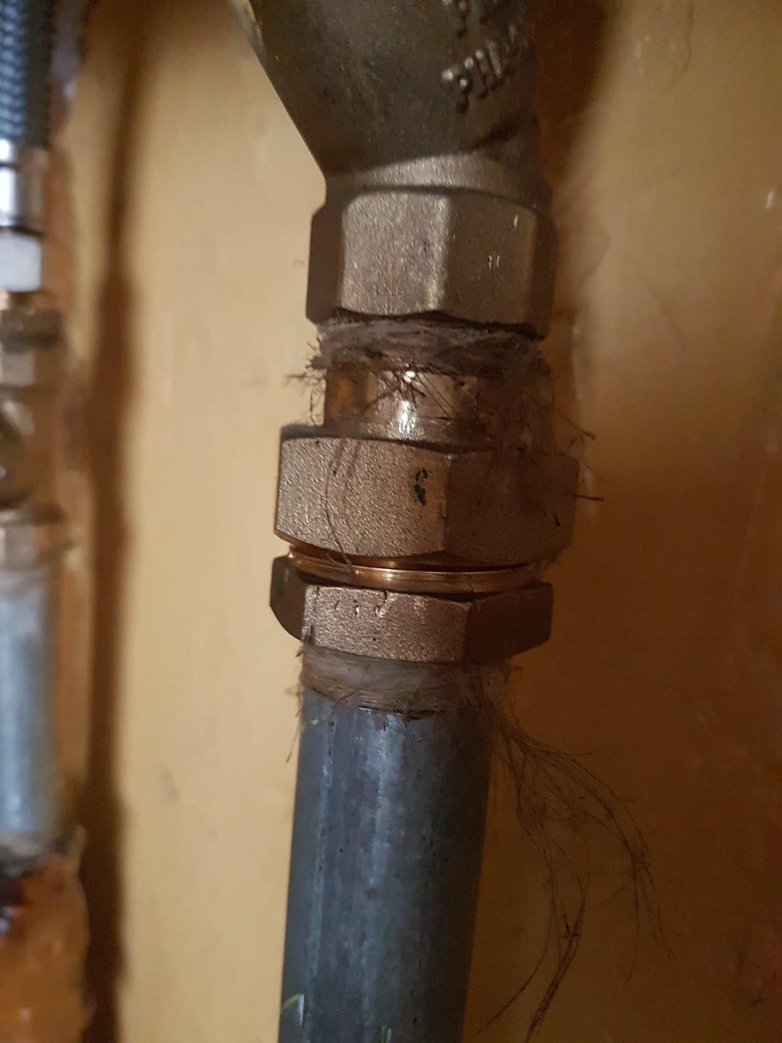 Mosiężne złączki instalacji gazowej z widocznymi śladami uszczelniania oraz zabrudzeniami na tle beżowej ściany.