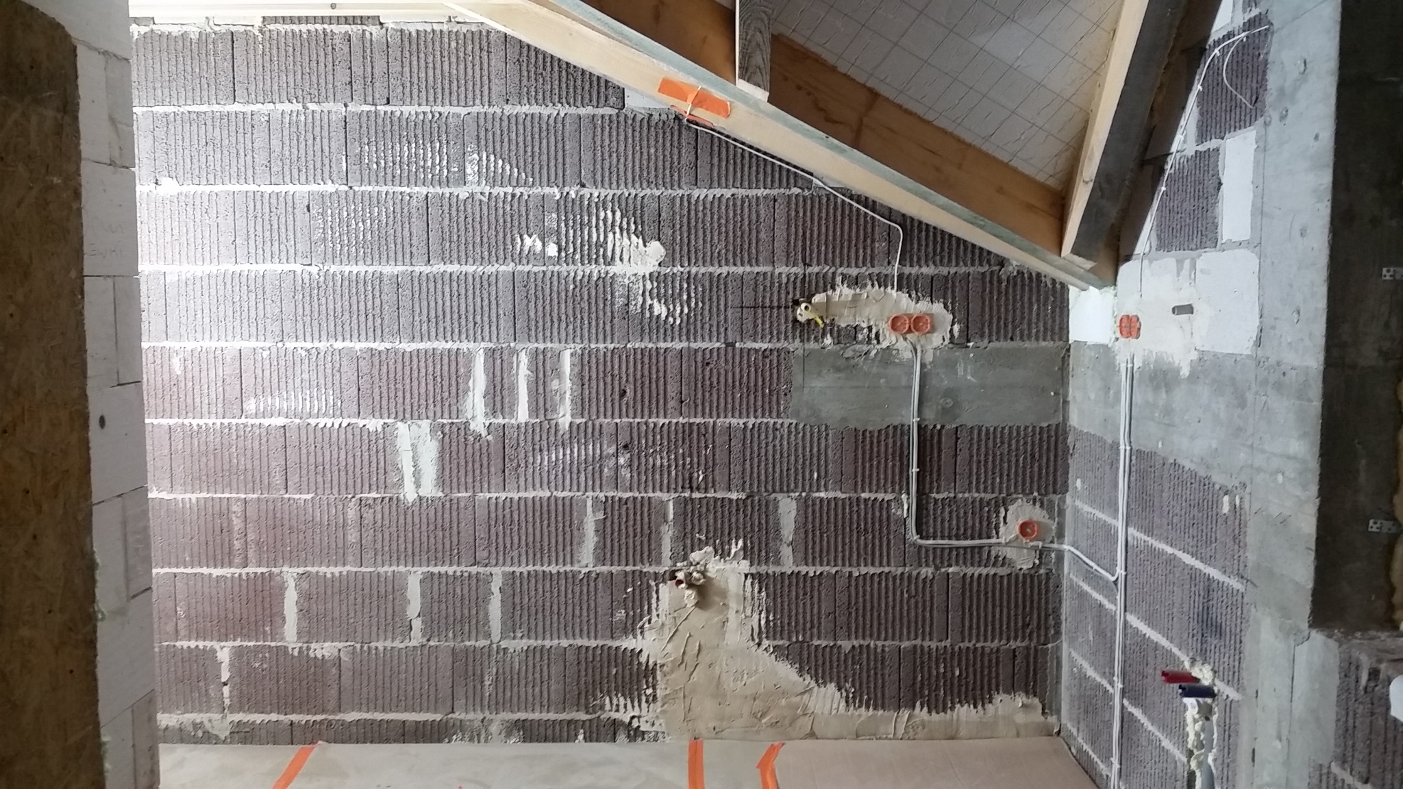 Surowy stan poddasza z widocznymi kablami elektrycznymi w peszlach i puszkami instalacyjnymi w ścianach z betonu komórkowego, przygotowanymi do dalszych prac wykończeniowych.