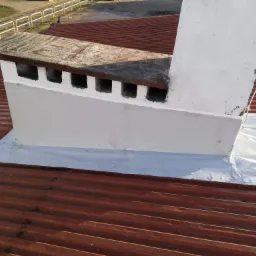 Czerwony dach z blachy trapezowej z kominem, który został uszczelniony białą folią i pomalowany na biało.