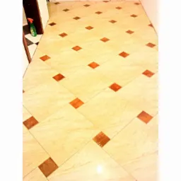 Jasne płytki podłogowe z brązowymi wstawkami ułożone w karo. W rogu butelka ze środkiem czyszczącym. Widok z góry.